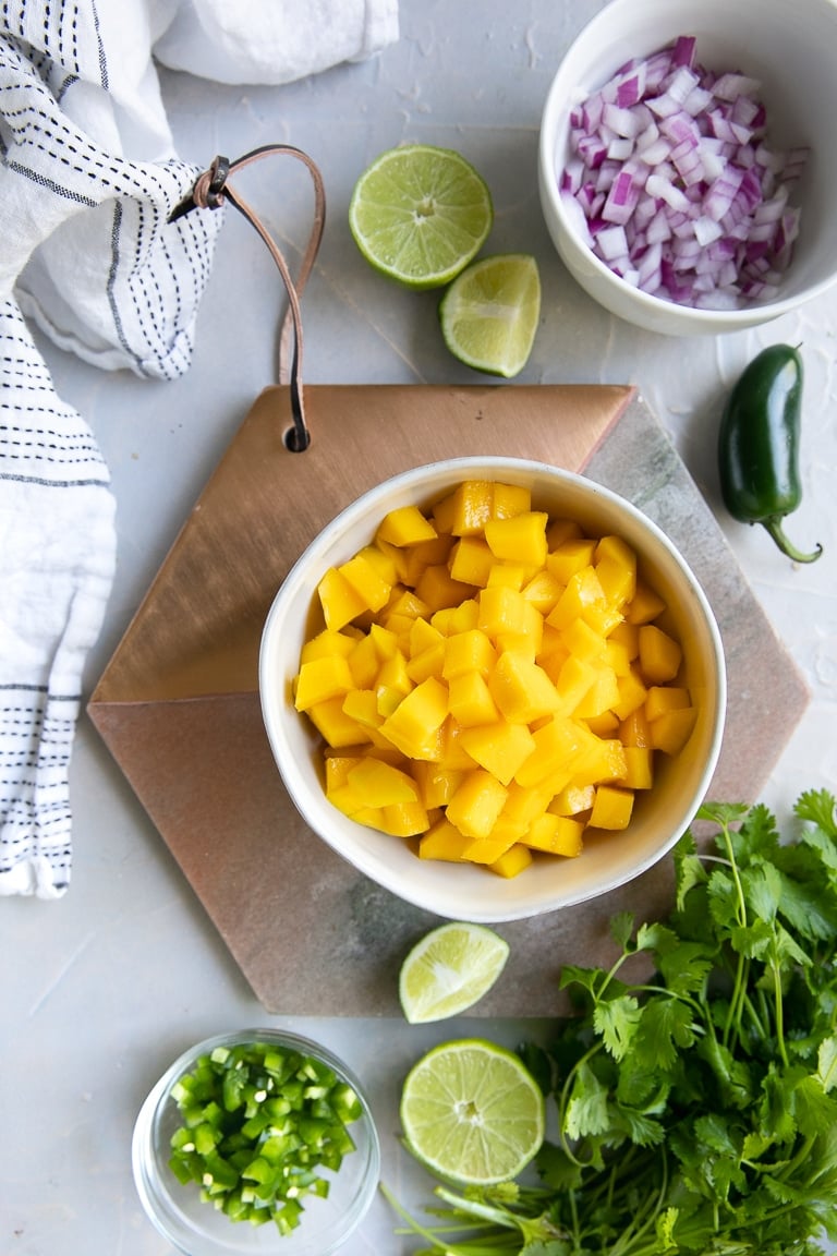 Overhead view of the ingredients needed to make mango salsa including chopped red onion, chopped mano, fresh cilantro, and limes.