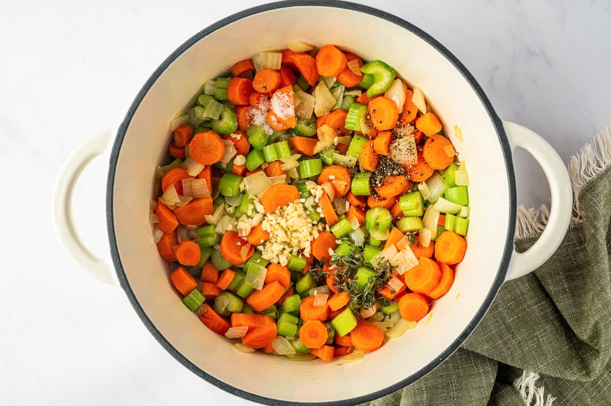 Sauteed carrots, celery, and onions topped with minced garlic, fresh thyme, salt, and cracked black pepper in a Dutch oven.