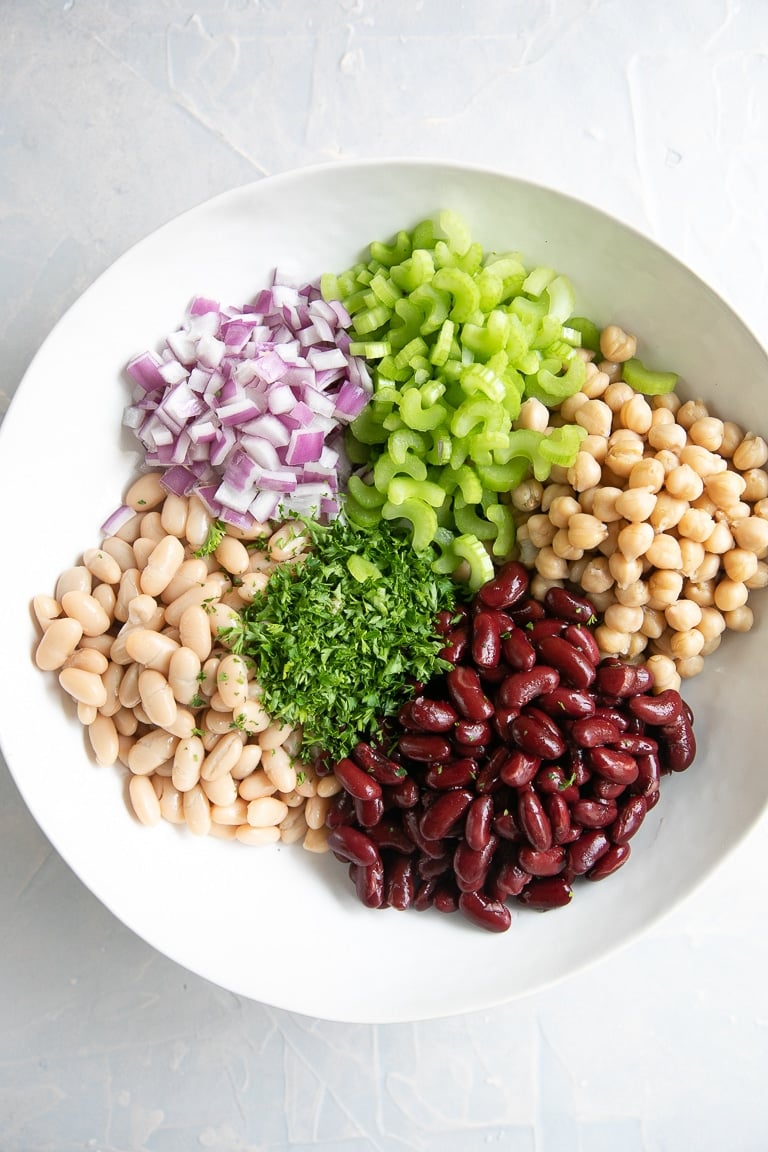 White bowl filled with chickpeas, kidney beans, parsley, celery, and red onion.