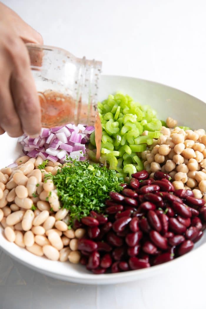 Pouring a light vinaigrette into a bowl filled with ingredients for an easy three bean salad.