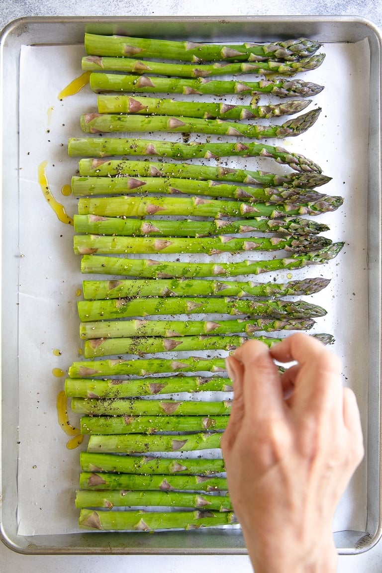 Seasoning a tray of asparagus before baking.