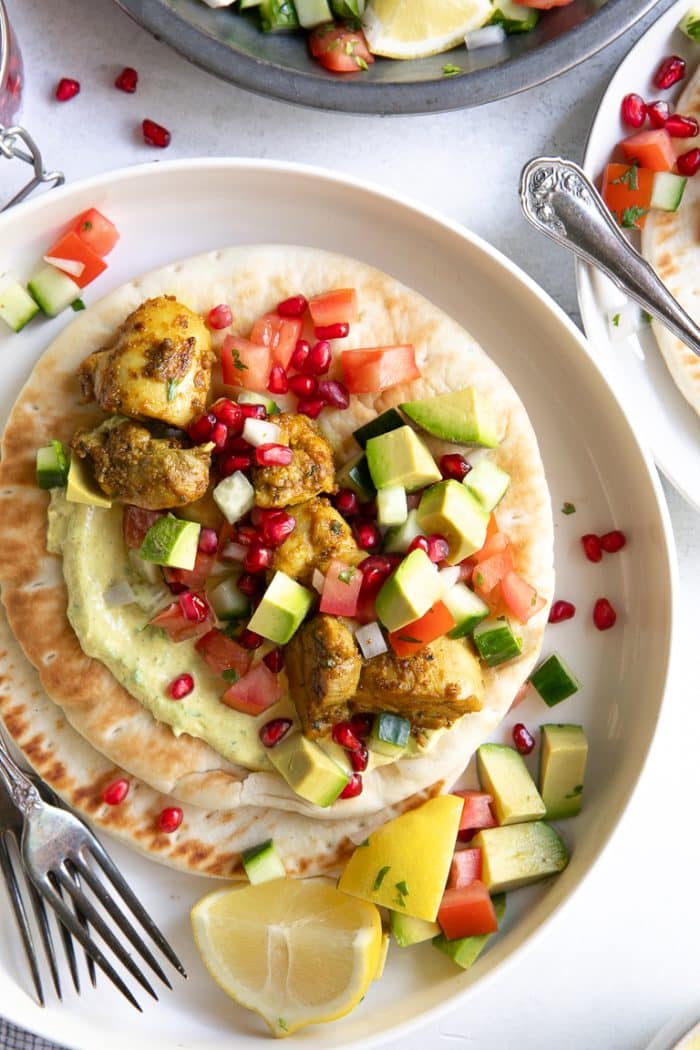 Overhead image of tandoori chicken gyros with avocado pomegranate salsa on a while plate.