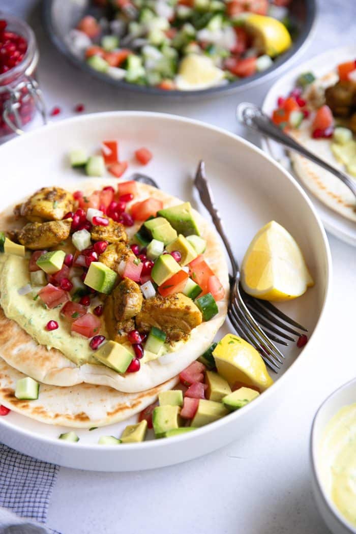 Tandoori chicken gyros with avocado pomegranate salsa on a while plate.