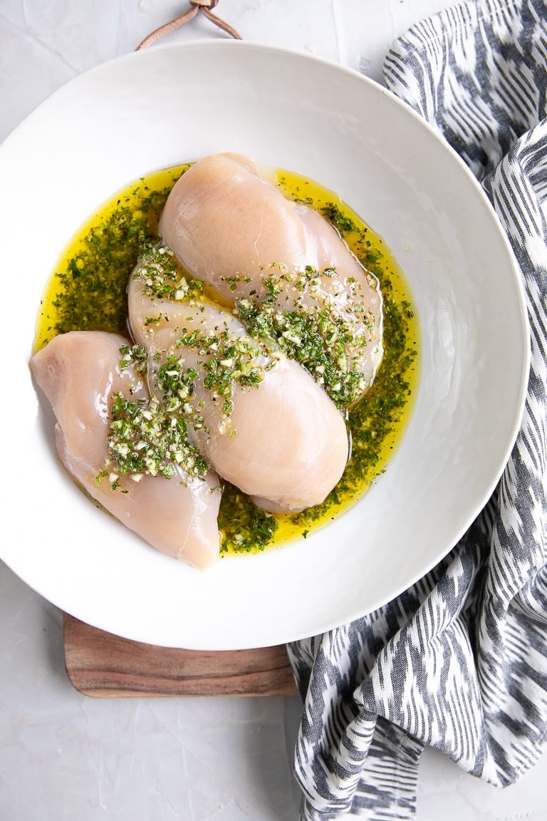 Three chicken breasts in a large shallow bowl marinating in homemade Greek marinade.
