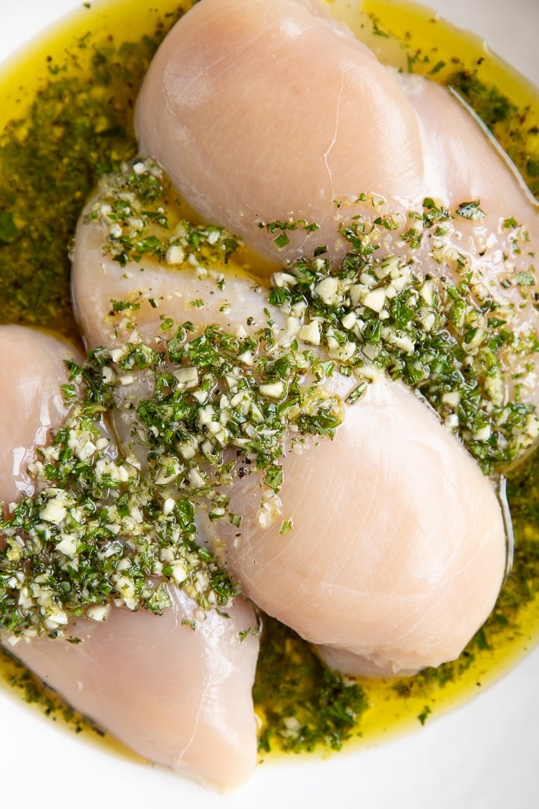 Three chicken breasts in a large shallow bowl marinating in homemade Greek marinade.