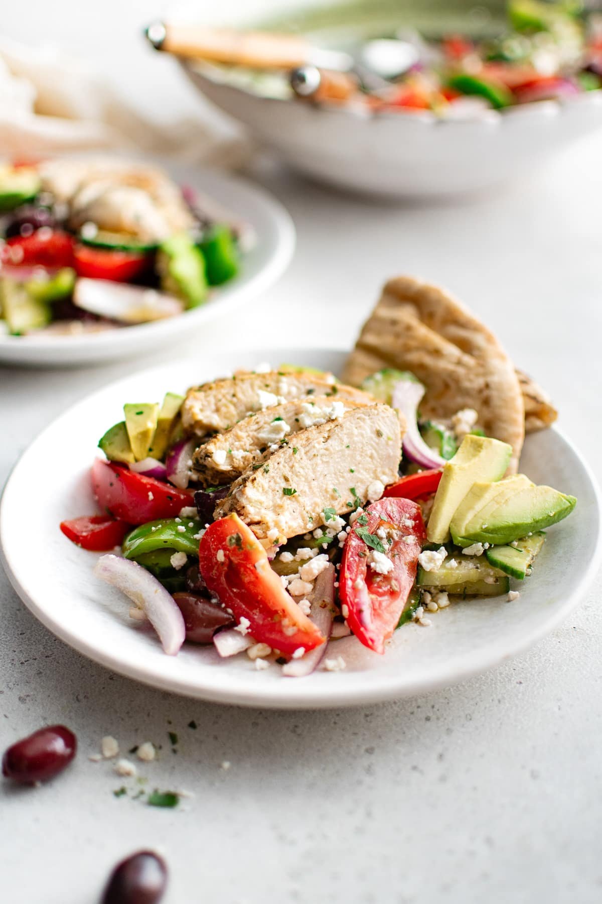 Sliced Greek chicken salad served with pita bread and avocado on a white plate.