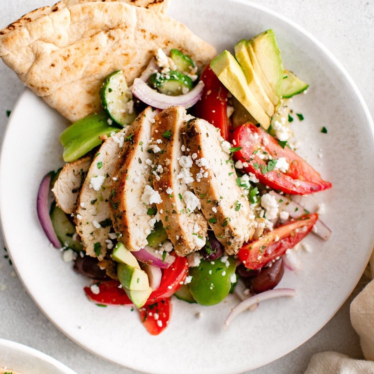 Overhead close-up of Greek Chicken Salad with sliced chicken, feta cheese, avocado, and pita.