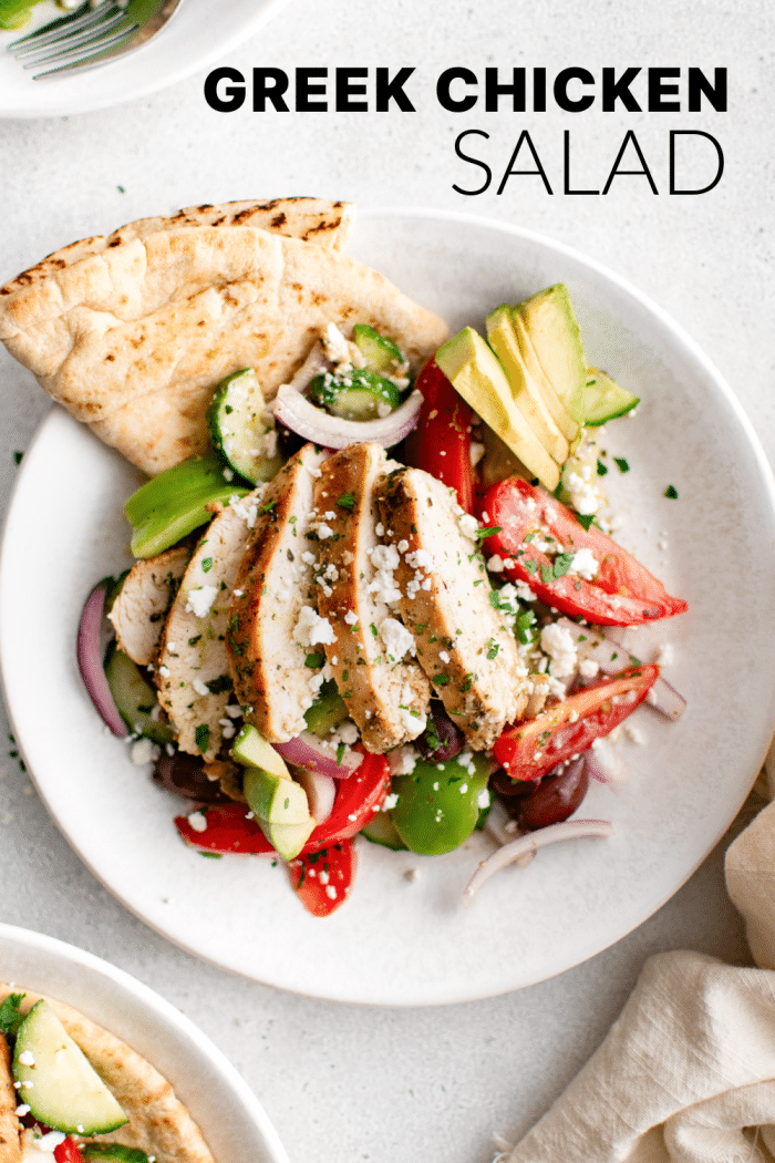 Overhead shot of sliced Greek chicken salad with avocado and pita on a white plate.