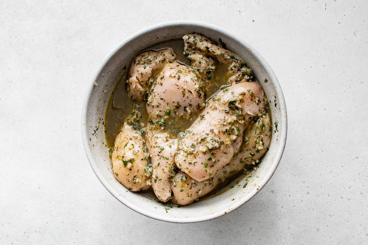Marinated chicken breasts coated in garlic, herbs, and olive oil, ready to be cooked for a fresh and flavorful salad.