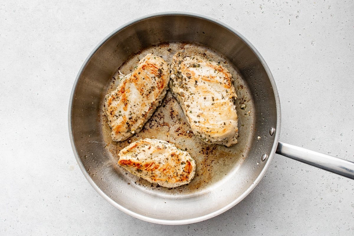 Juicy Greek-marinated chicken breasts cooking to golden perfection in a skillet—crispy edges, tender center.