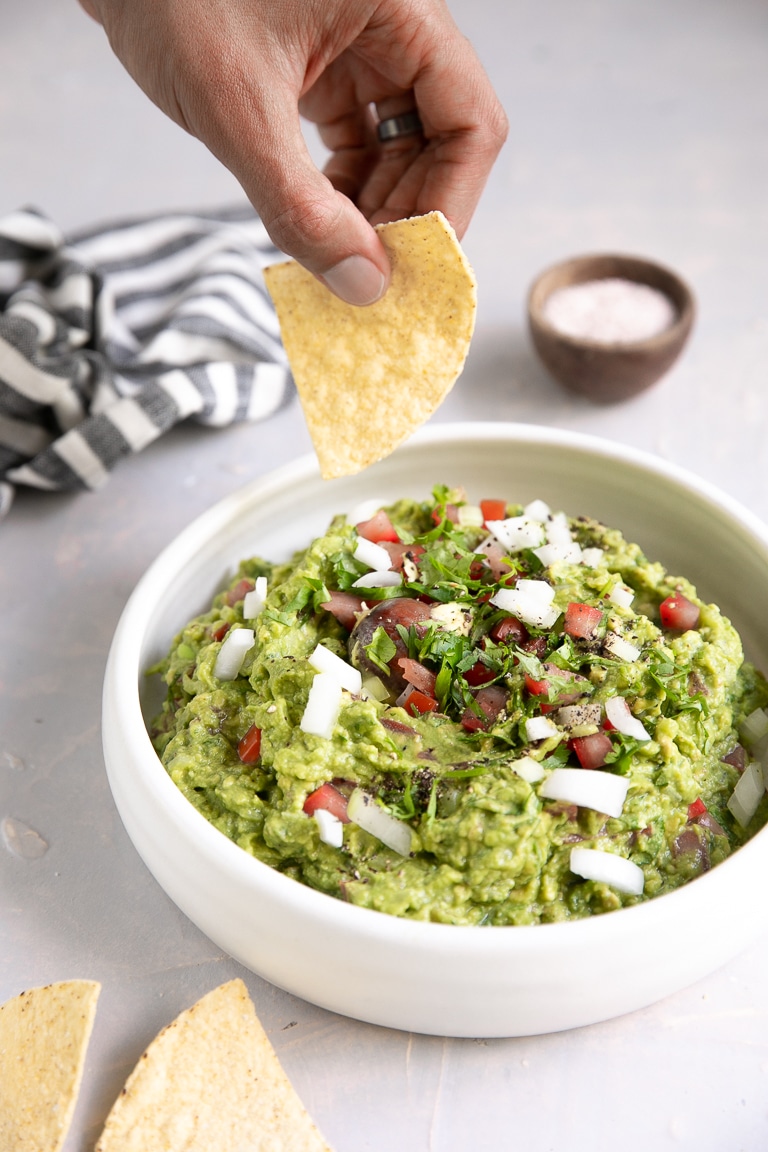 Hand dipping a chip into homemade fresh guacamole.