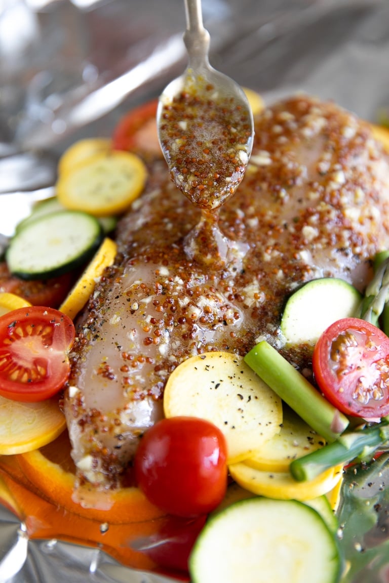 Raw chicken breast in foil being covered in honey mustard sauce.