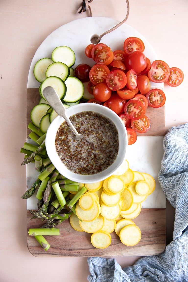 Overhead image of a serving tray with prepared honey mustard sauce and raw squash, cherry tomatoes, and asparagus.