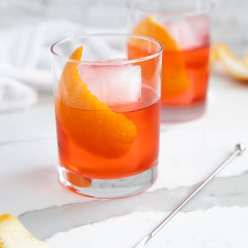 Two Negroni cocktails in a rocks glass garnished with orange peel.