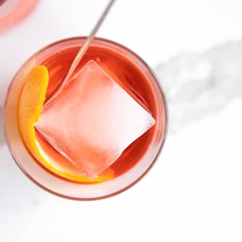 Overhead image of a negroni served in a rocks glass with a single large square ice cube and orange peel.