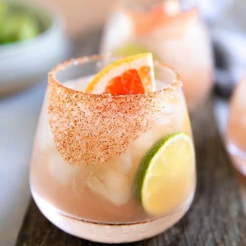 Paloma cocktail served with a chili salt rim and garnished with lime and fresh grapefruit.
