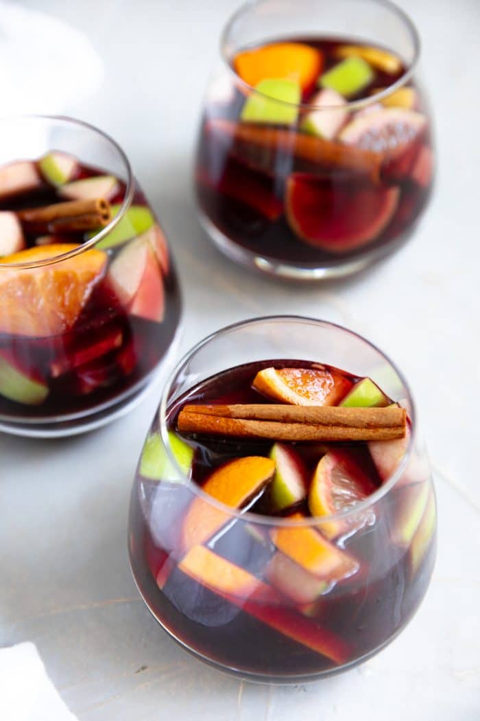 Three glasses of sangria made with red wine, oranges, lemon, apples, and cinnamon stick.
