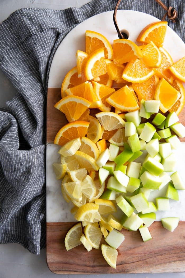 Cutting board with sliced oranges and lemons and chopped granny smith apples.