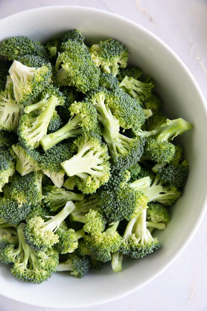 Large white bowl filled with raw broccoli florets.