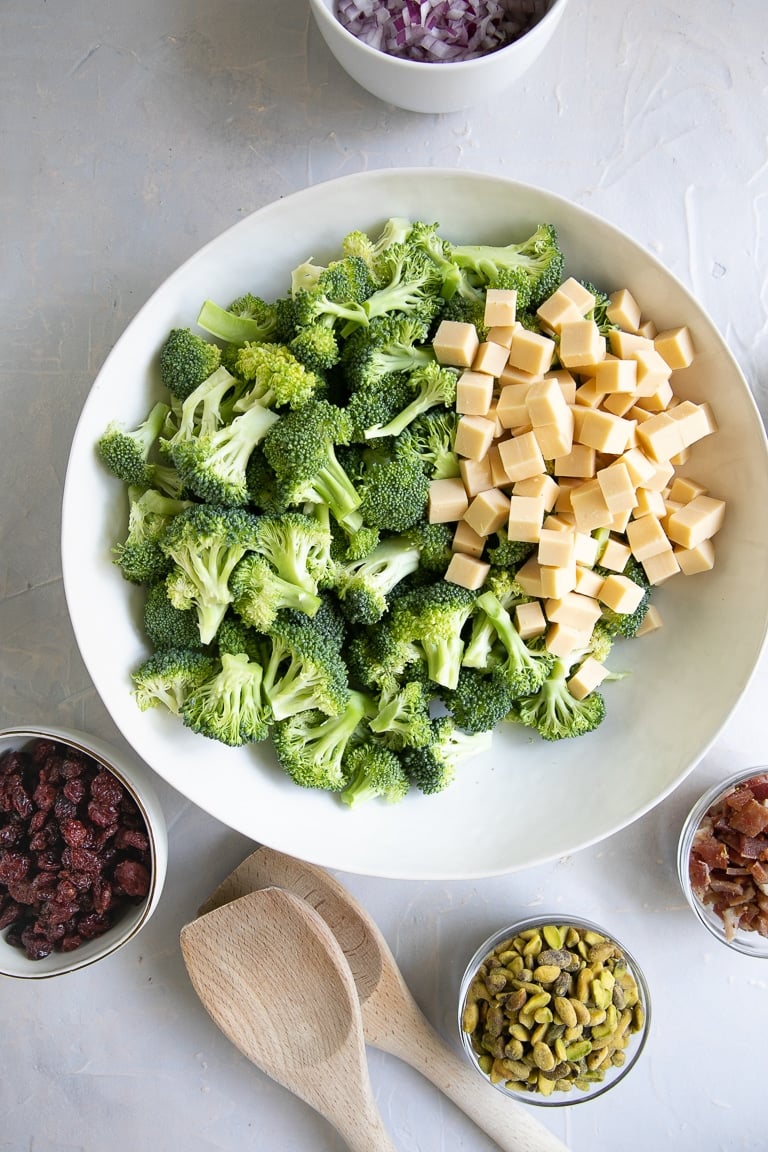 Large white bowl filled with raw broccoli florets and cubed smoked gouda cheese.