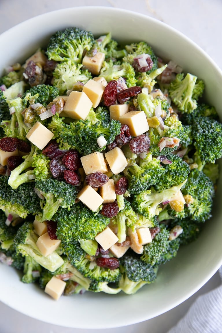 Large bowl filled with mixed together broccoli salad with creamy mayo dressing, bacon, and cranberries..