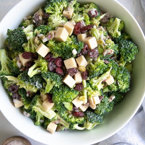 Large bowl filled with mixed together broccoli salad with creamy mayo dressing, bacon, and cranberries..