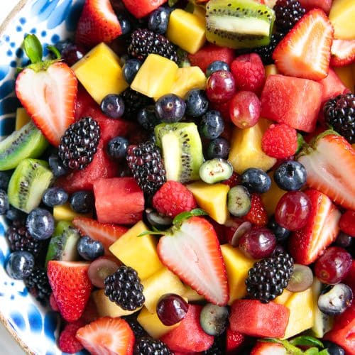 Large salad bowl filled with a variety of different fresh fruit including blackberries, ,strawberries, grapes, pineapple, kiwi, and watermelon.