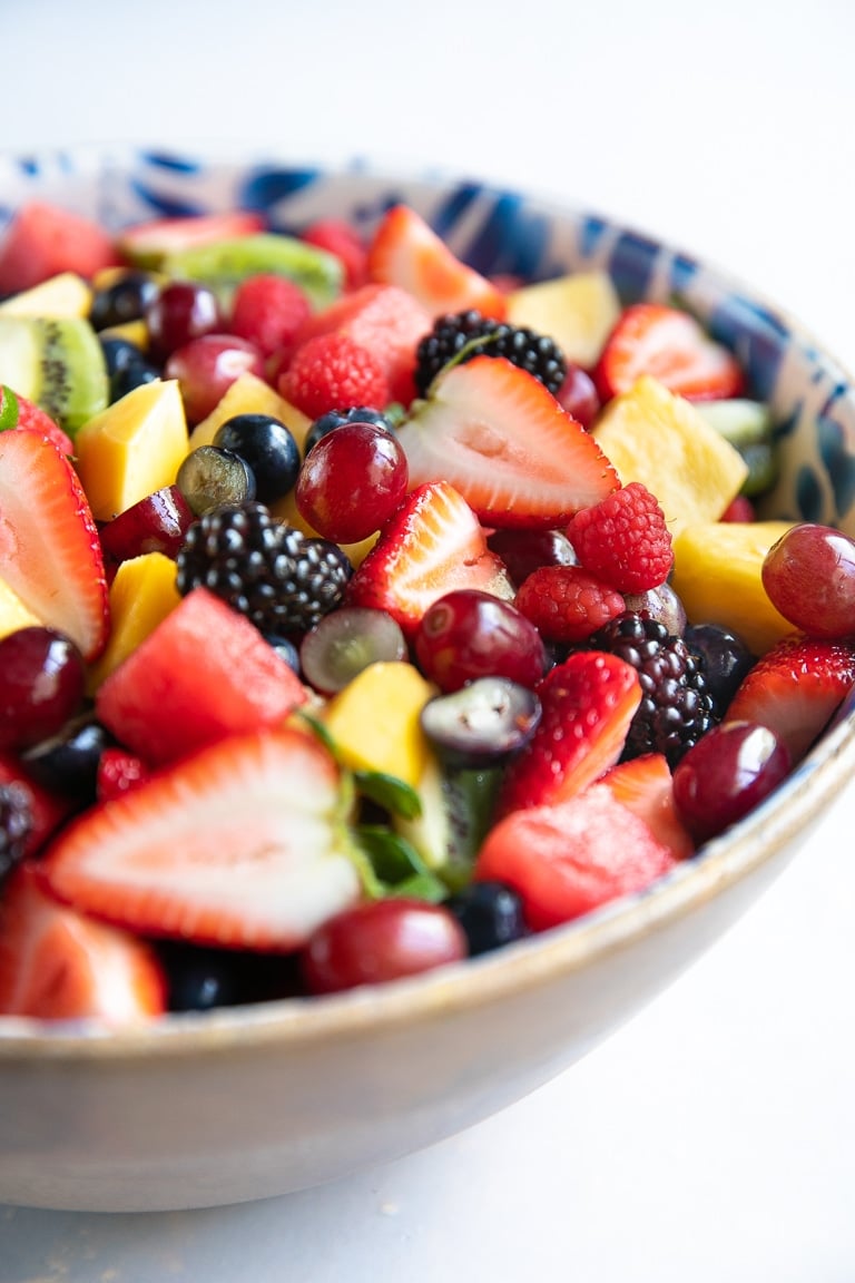 Large salad bowl filled with a variety of different fresh fruit including blackberries, ,strawberries, grapes, pineapple, kiwi, and watermelon.