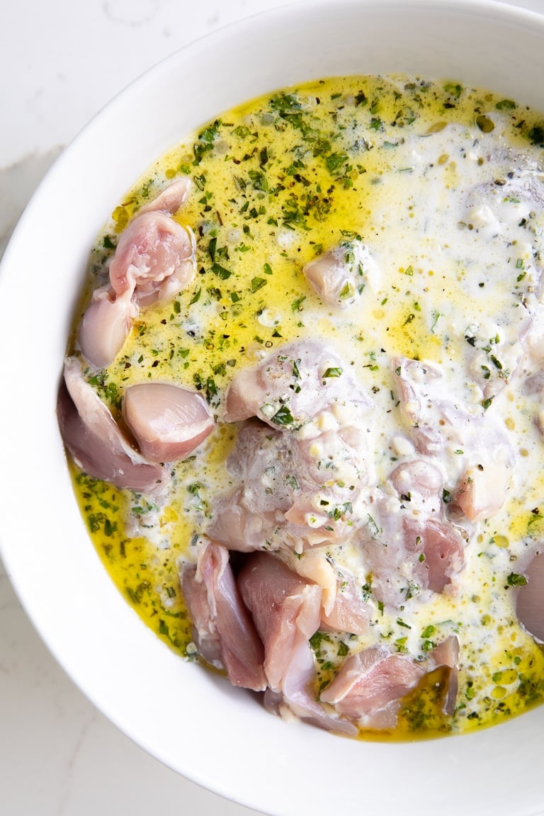 Chicken marinating in yogurt, lemon, garlic, olive oil, and fresh herbs.