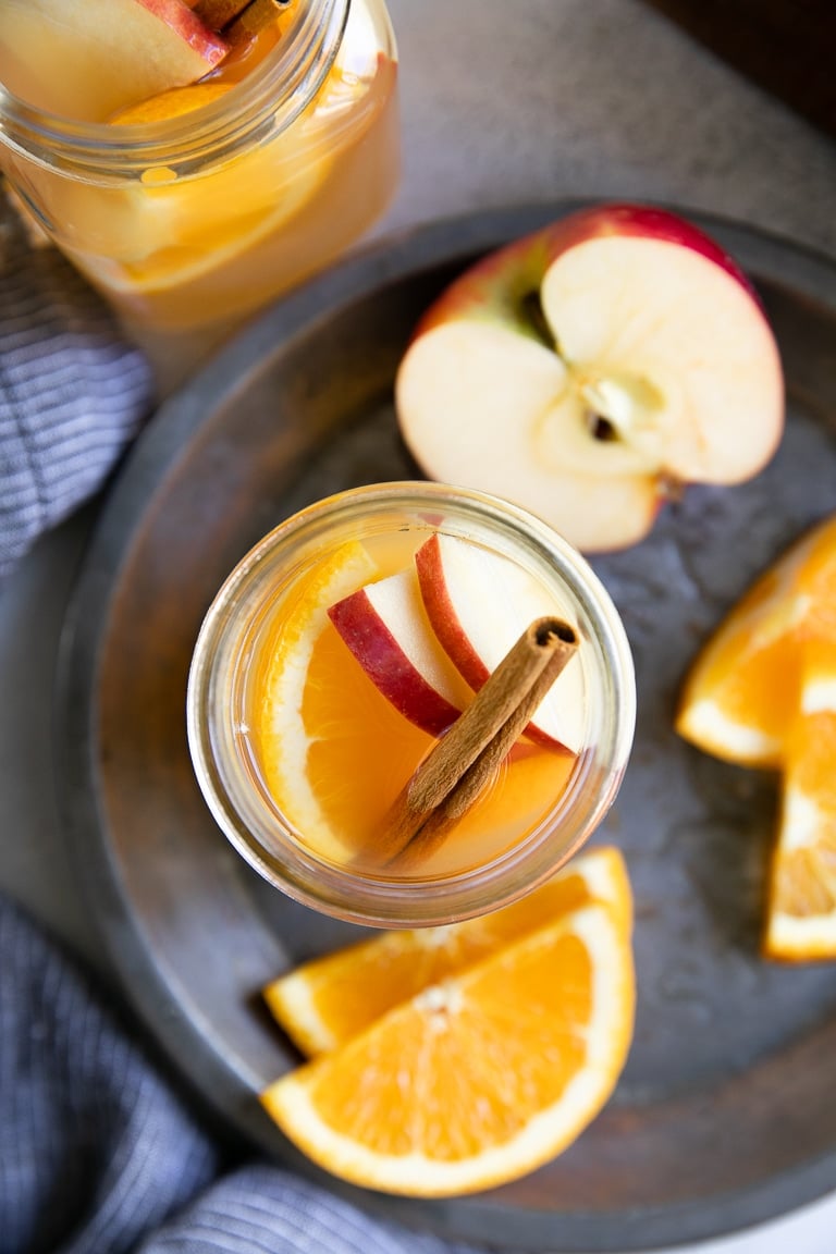 Overhead image of two jars filled with apple cider and garnished with fresh apples and orange slices.