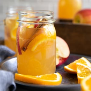 Mason jar filled with warm homemade apple cider garnished with sliced apples, oranges, and cinnamon stick.
