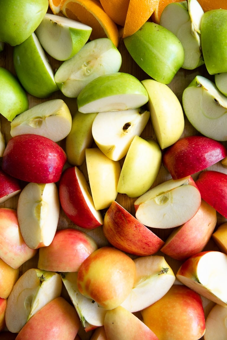 Different types of sliced apples quartered and layed out on a large cutting board.