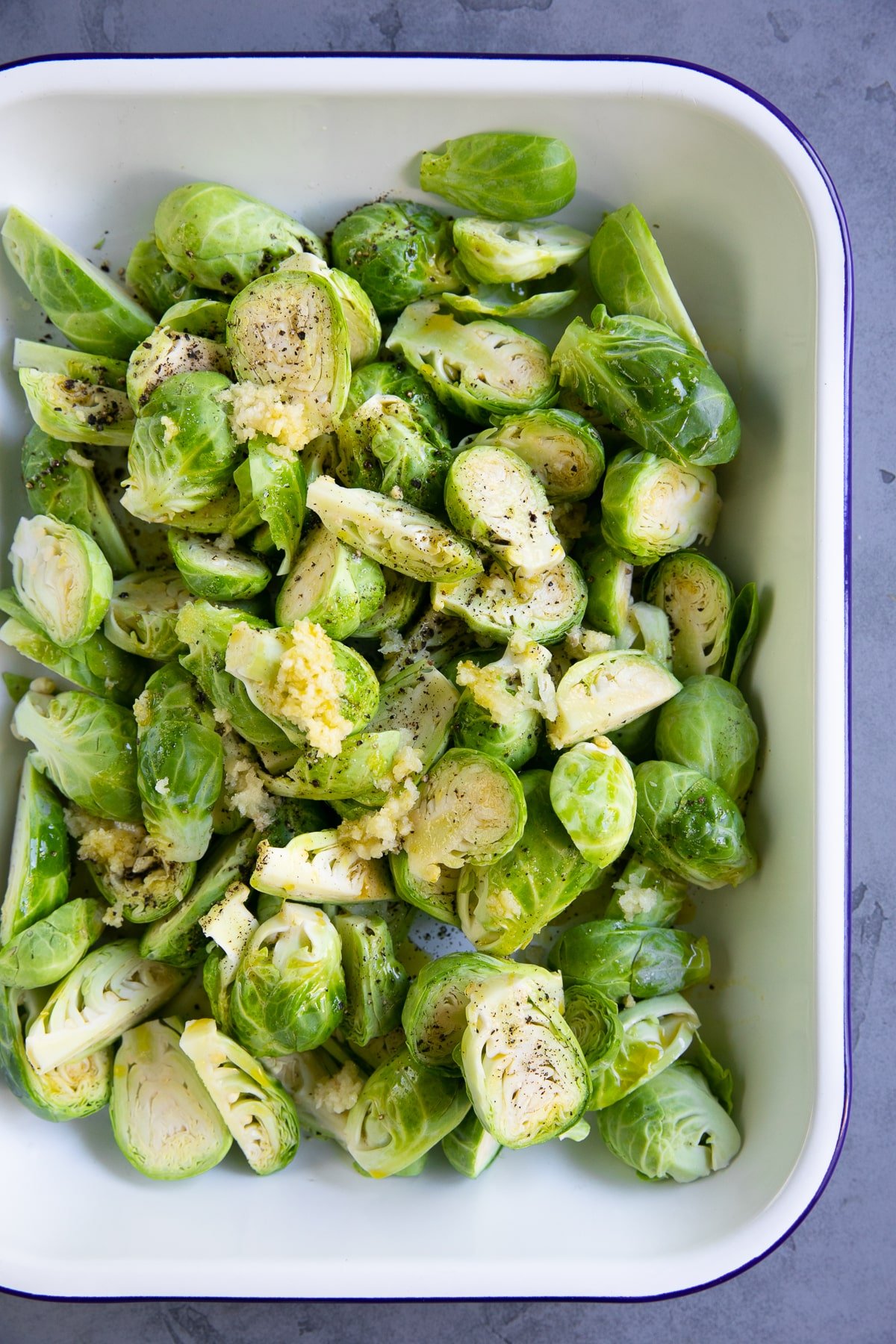Raw Brussels sprouts sliced in half and drizzled with olive oil, minced garlic, salt, and pepper.