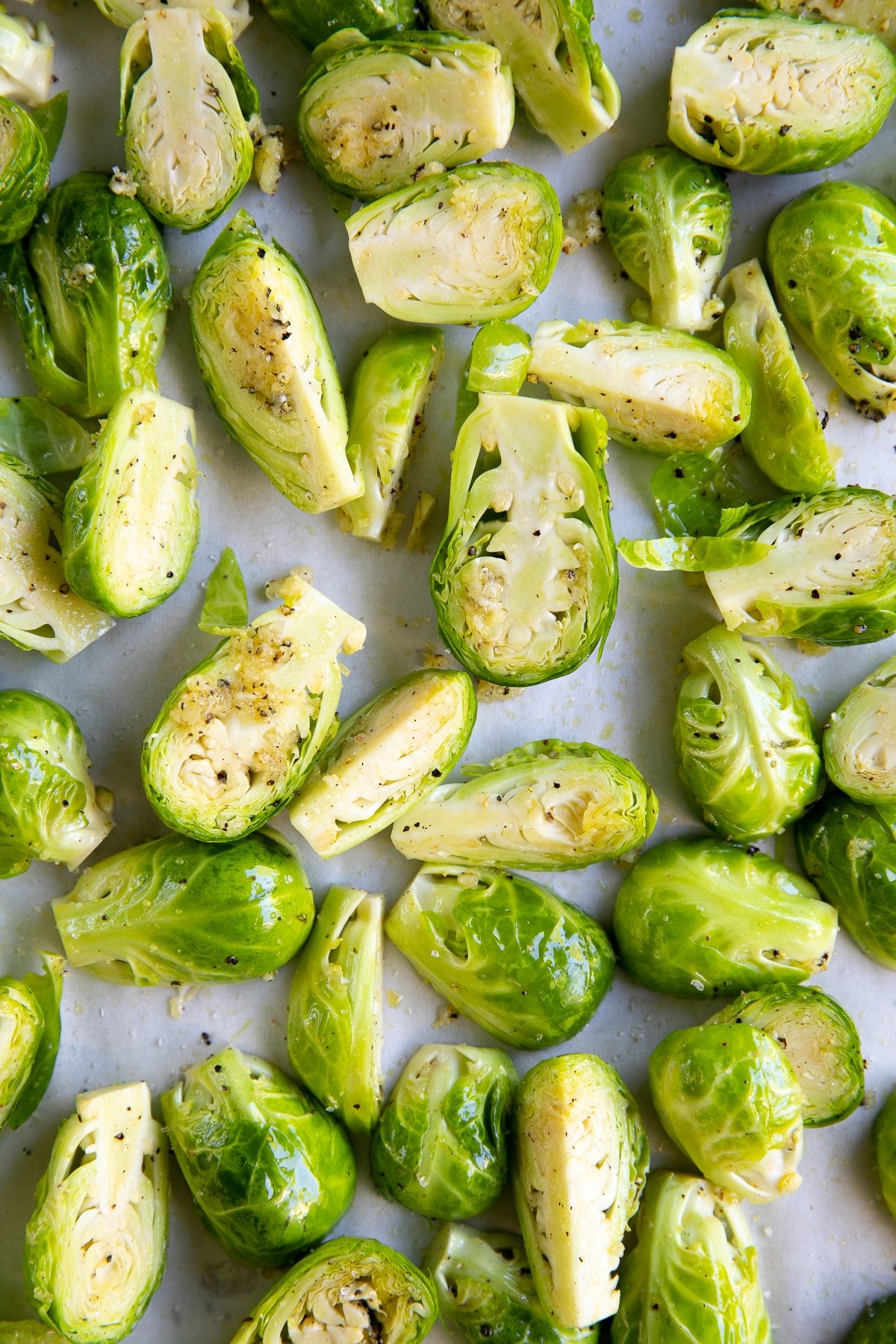 Raw Brussels sprouts sliced in half, tossed in olive oil and garlic, and set out in an even layer over a large baking sheet.