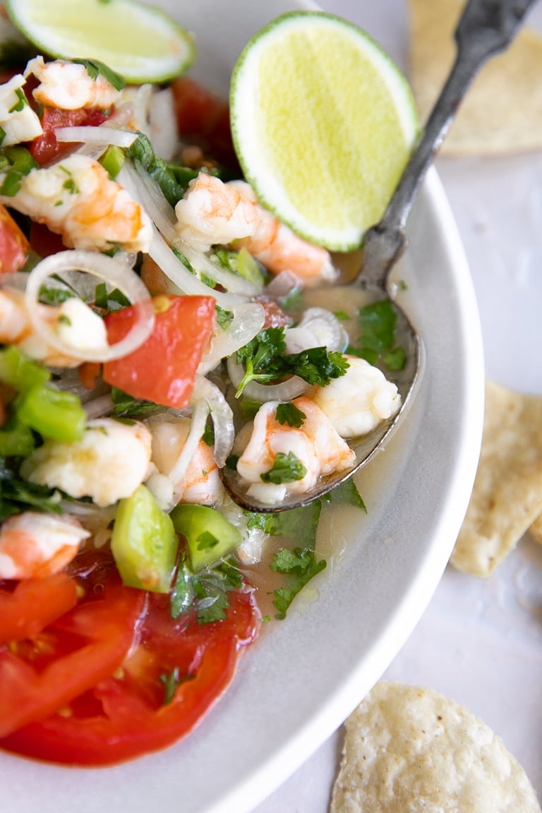 Spoon resting in a white dish filled with fresh shrimp ceviche.