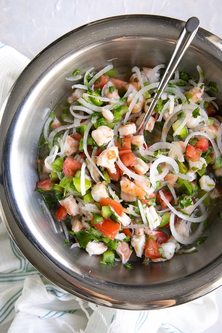 Large mixing bowl filled with shrimp, sliced onion, bell pepper, tomatoes, cilantro, and citrus juice.