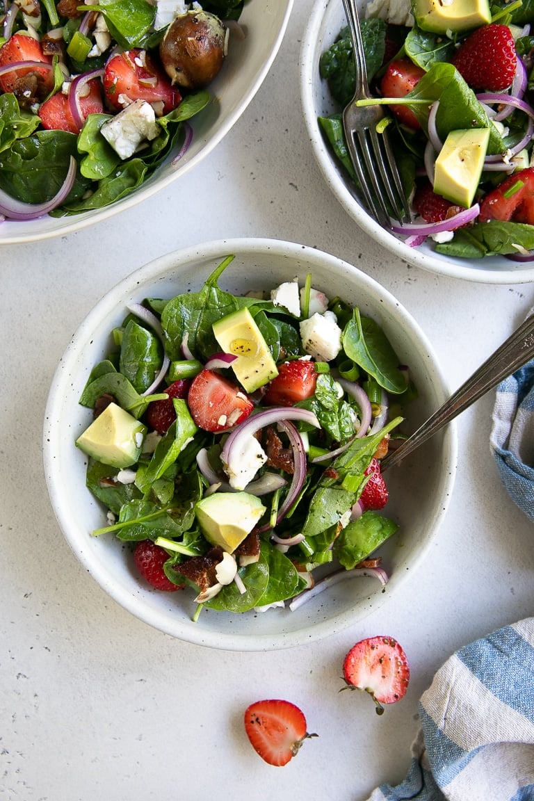 Three single serving salad bowls filled with strawberry spinach salad and drizzled with lime vinaigrette.