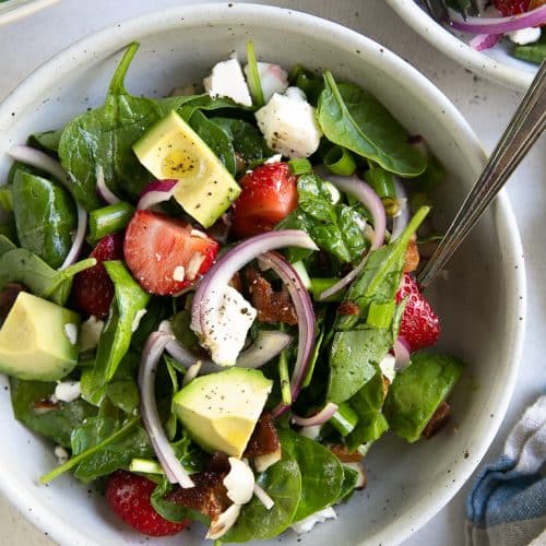 SIngle serving salad bowl filled with strawberry spinach salad.