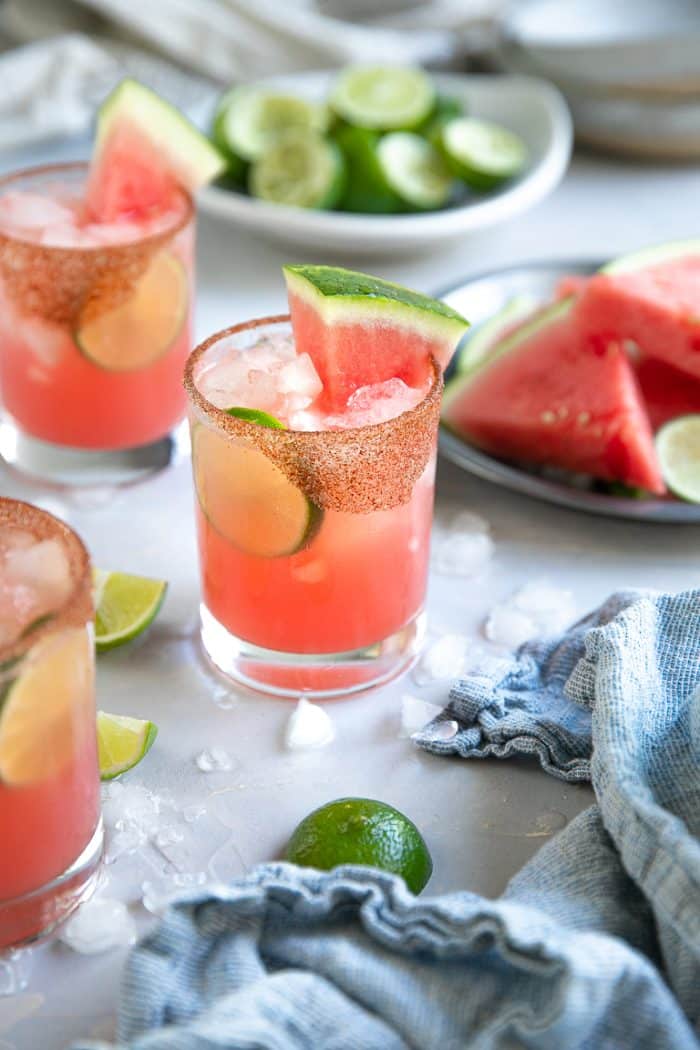 Three iced watermelon margaritas in rocks glasses garnished with fresh lime wheels and sliced watermelon.