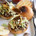 Spoon drizzling reduced apple cider sauce over the top of a toasted bun topped with shredded apple cider pulled pork and homemade apple coleslaw.