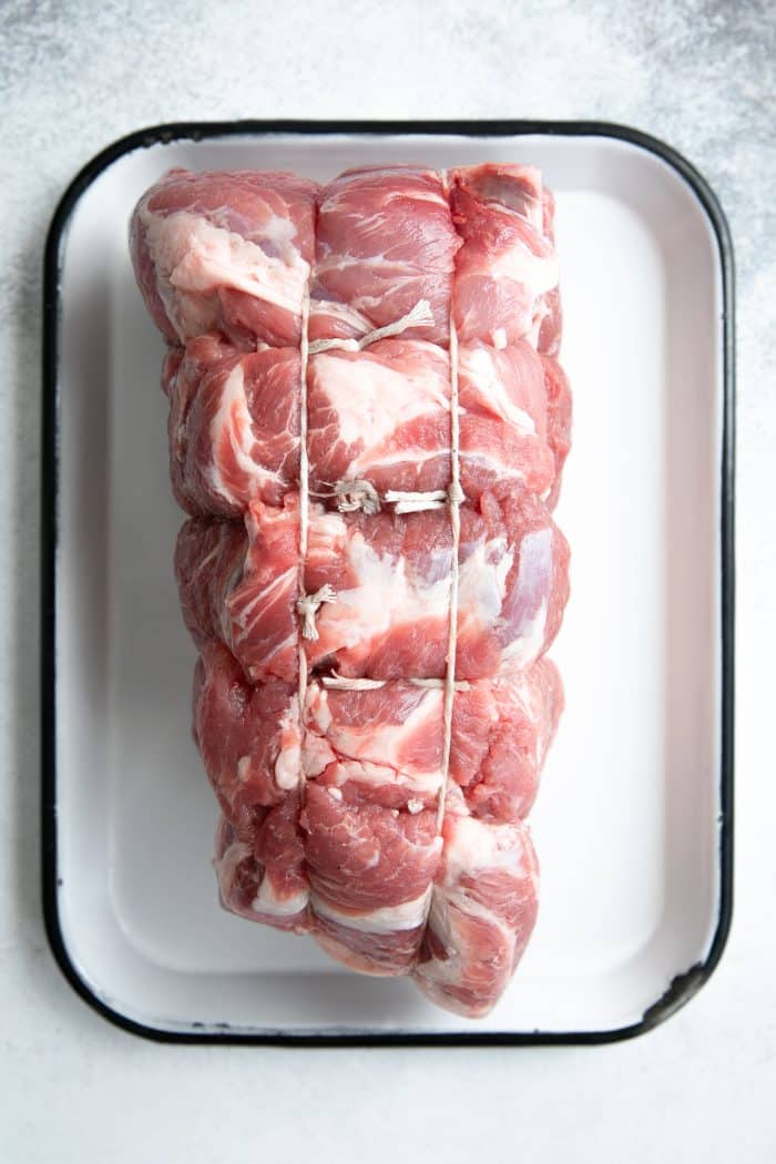 Trussed pork shoulder on a white baking sheet.