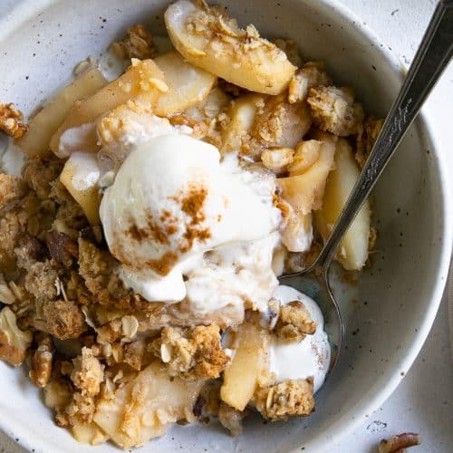Shallow serving bowl filled with apple crisp and topped with melting scoop of vanilla ice cream.