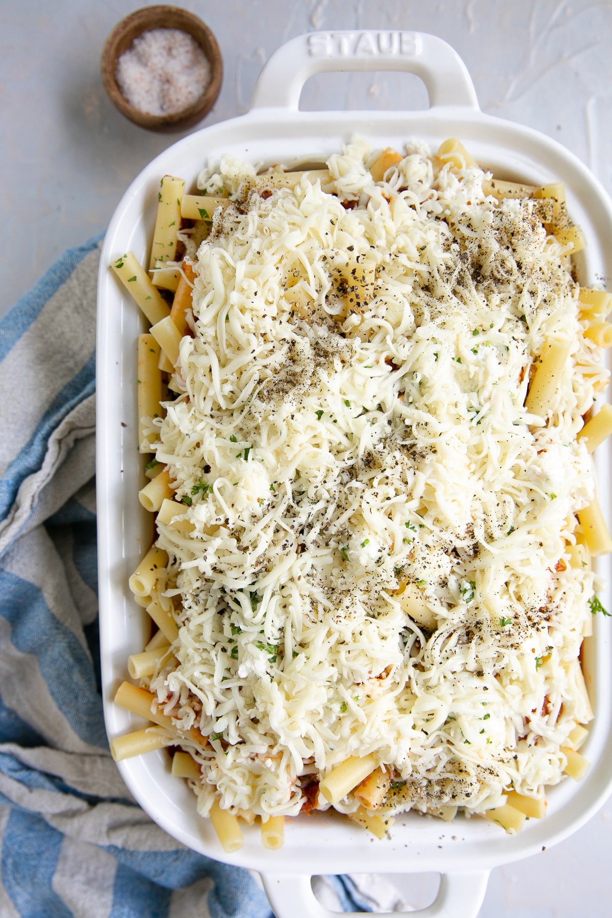 Layered white casserole dish filled with ziti noodles, tomato sauce, and shredded mozzarella cheese.