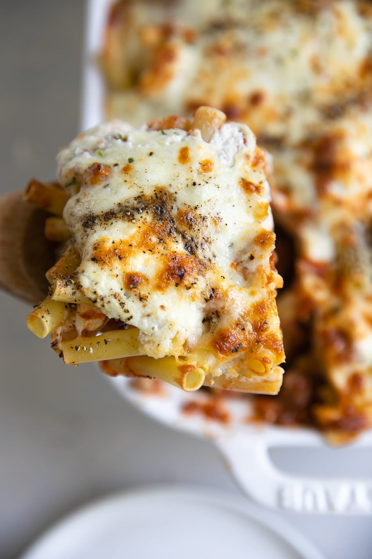 Wooden spoon holding a large scoop of baked ziti.
