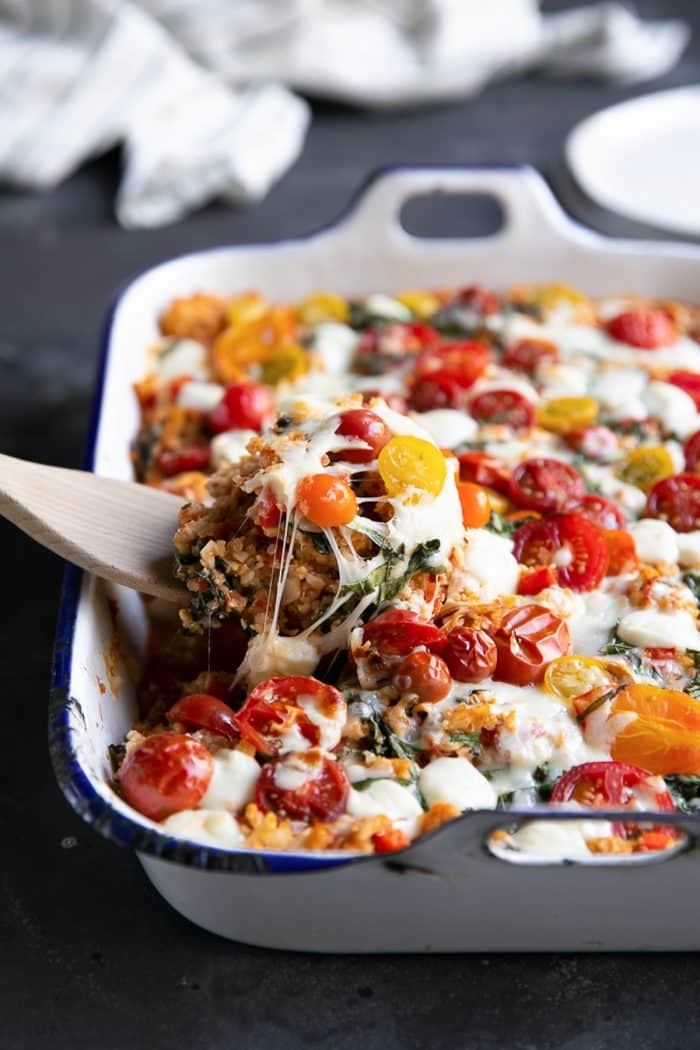 Wooden spatula scooping a spoonful of caprese casserole from a large white baking dish.