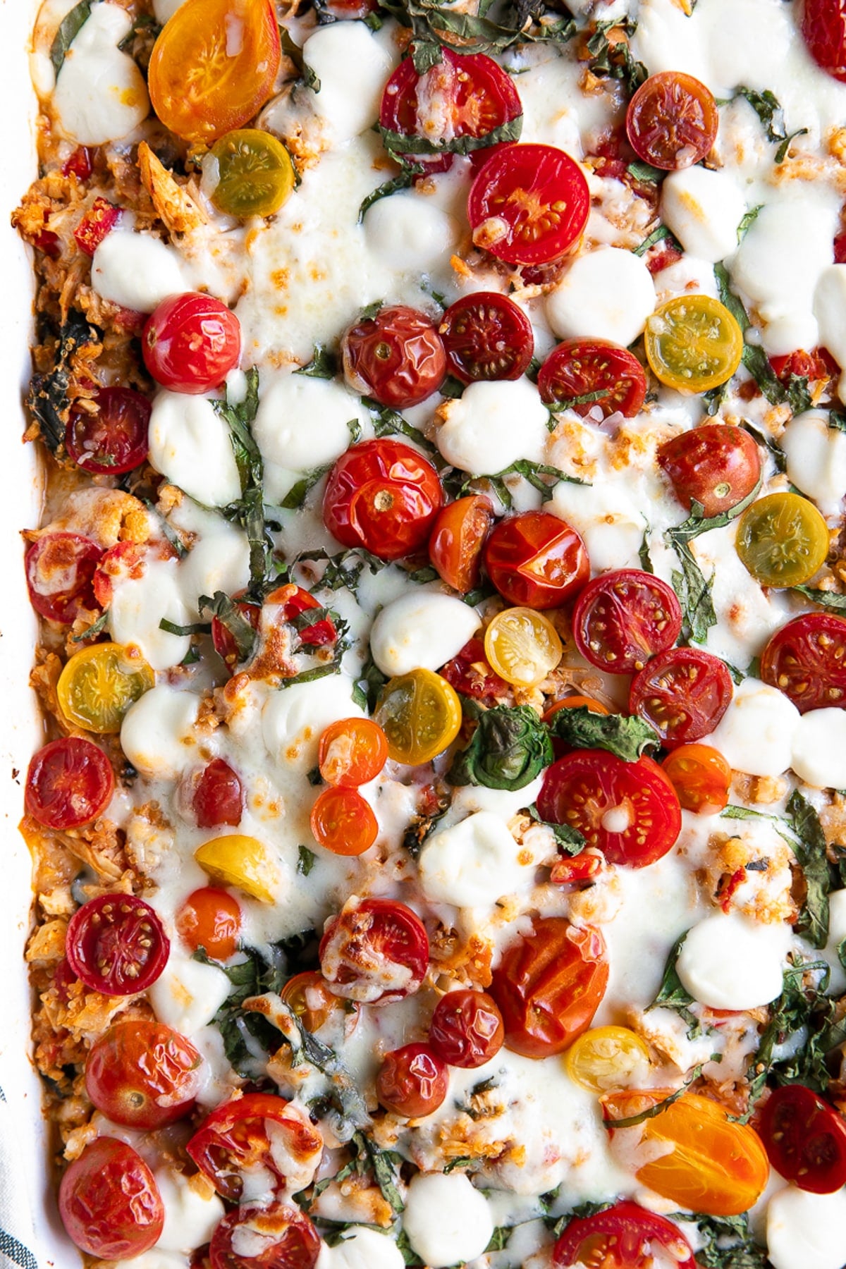 Overhead image of baked caprese casserole topped with cherry tomatoes and mozzarella pearls.