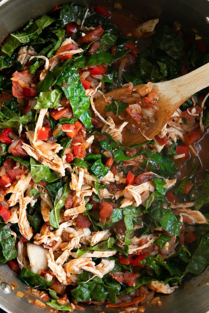 Large pot filled with cooked chicken, tomatoes, and kale.