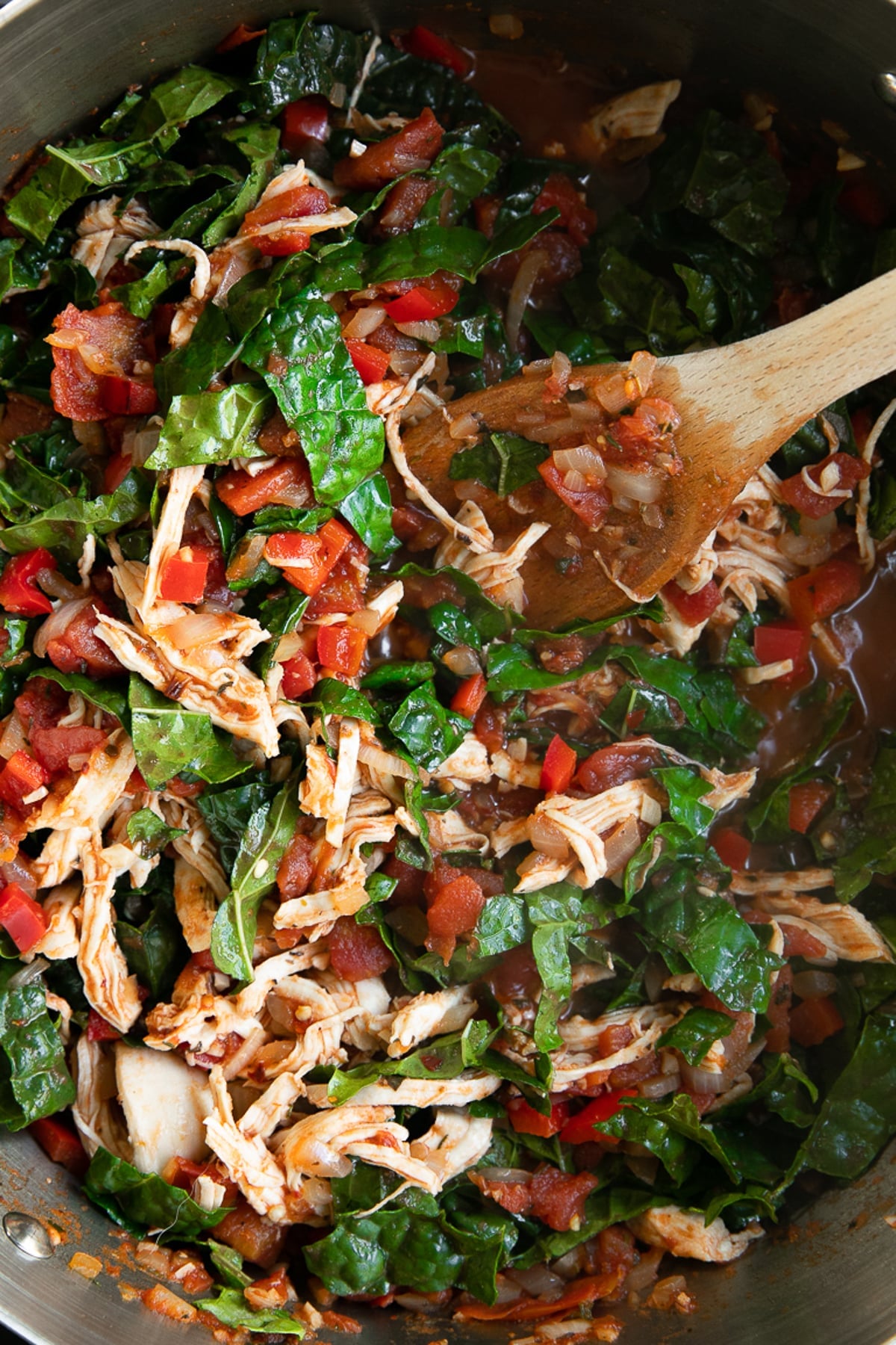 Large pot filled with cooked chicken, tomatoes, and kale.