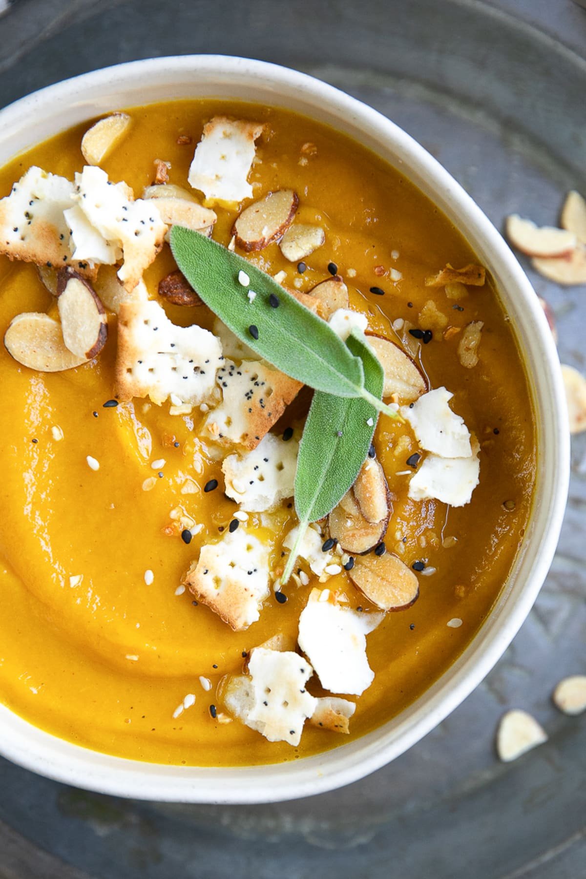 Bowl of acorn squash soup garnished with crackers, sesame seeds and fresh sage.