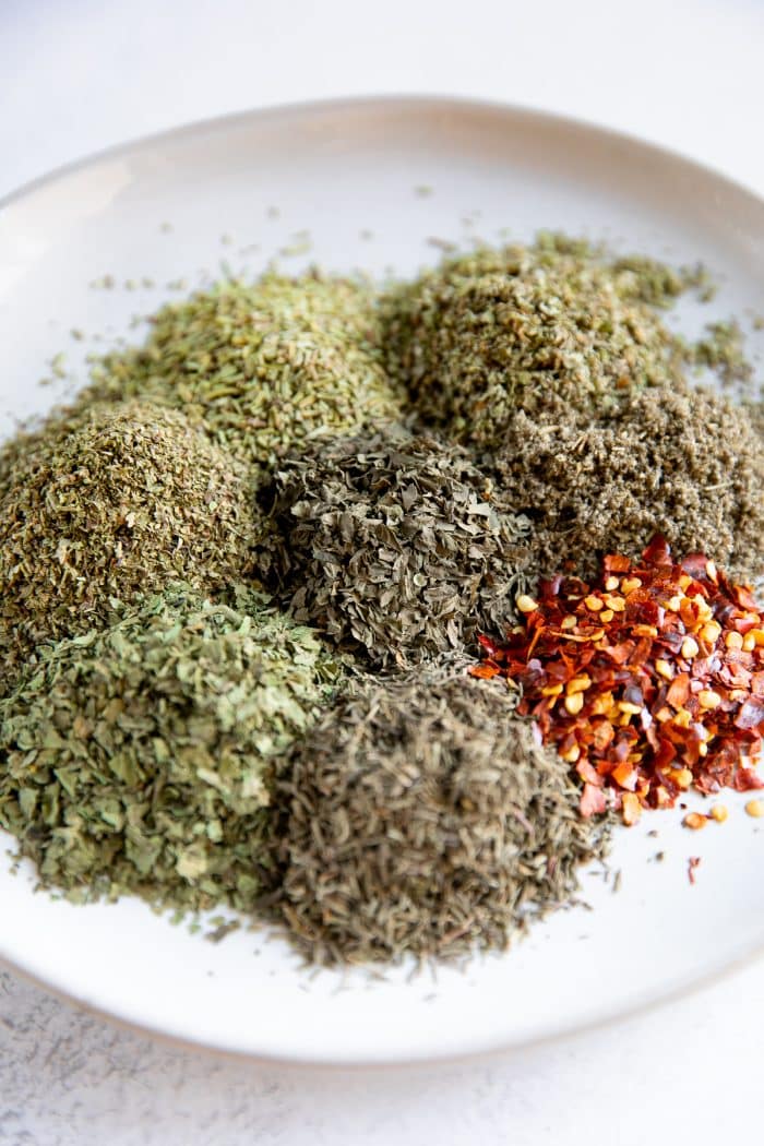 Piles of different dried herbs on a white serving plate.